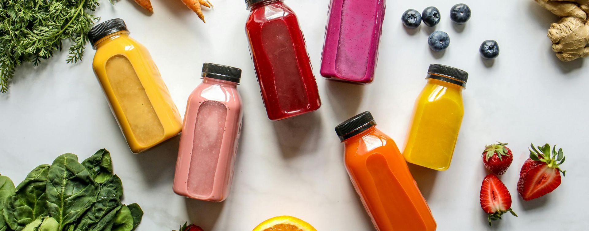 Colorful Bottles with Smoothies Beside Carrots, Ginger, Leaves and Berries